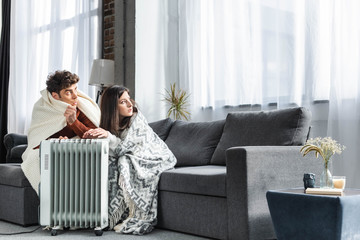 Fototapeta attractive girlfriend and boyfriend covered with blankest warming up near heater obraz