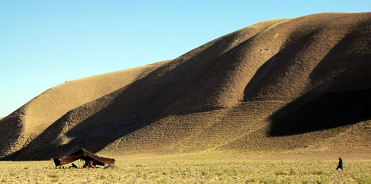 Countryside close to Bala Murghab in Badghis Province on the road to Maymana. Nomads have pitched a tent on the scrubby grassland beneath a hill. A woman walks towards the tent. Western Afghanistan.