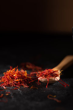 Saffron spices heap and wooden spoon on black slate stone table. Saffron flavor and coloring seasoning ingredient.