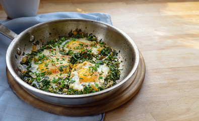 pan with spinach and fried eggs, spices and herb garnish, protein-rich dish for low carb diet on a...