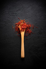 Saffron spices threads in wooden bamboo spoon on dark table flat lay top view. Saffron flavor and...