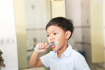 An Asian young boy brushing his teeth.