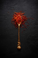 Saffron spices threads in vintage brass spoon on dark table flat lay top view. Saffron flavor and...