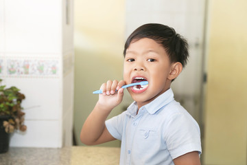 An Asian young boy brushing his teeth.