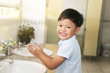 An Asian school boy washing his hand at a faucet sink and water tab in a school. 