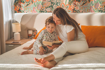 Pretty young mother reading a book to her little son in modern interior