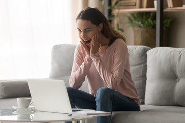 Amazed girl feeling great surprise looking at laptop at home
