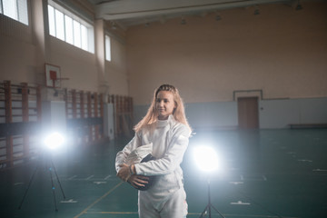 A portrait of a young woman fencer holding her helmet at the school gym