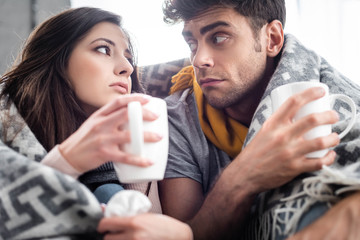 sick girlfriend and boyfriend covered with blanket holding cups of tea