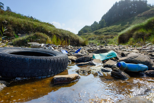 Earth plastics pollution global enviroment emergency. Old car tire in dirty water with plastic bottles and trash.