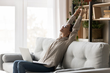 Happy woman stretching sit on comfortable couch with laptop