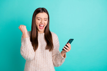 Portrait of cheerful delighted girl read news from her cell phone scream yeah raise fists isolated...