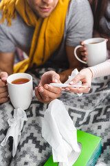 cropped view of sick girlfriend and boyfriend holding cups and thermometer