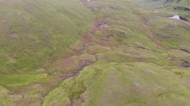 An aerial forward downward footage of a grassy mountain plateau rocky summit with small dry pond 