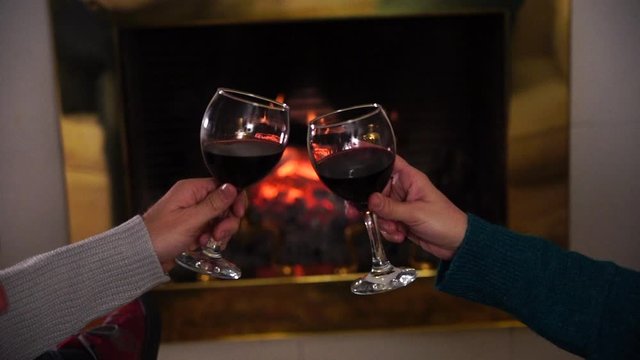 Close up of romantic couplemaking a toast with red wine celebrating happy moments together. Romantic background fireplace in winter holiday vacation, Christmas, valantine or anniversary.
