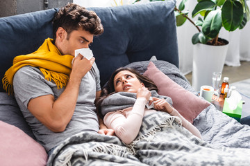 sick girlfriend and handsome boyfriend sneezing and holding napkins