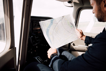 partial view of pilot sitting in plane and holding map