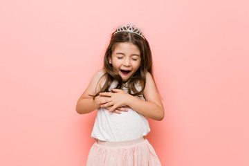 Little girl wearing a princess look laughs happily and has fun keeping hands on stomach.