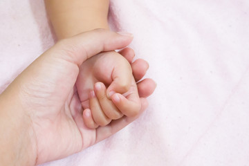 Obraz na płótnie Canvas Mother holding baby hand on soft pink background