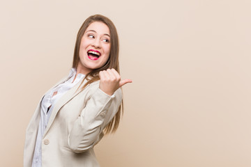 Young business woman points with thumb finger away, laughing and carefree.