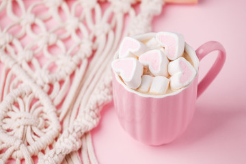 Cup of hot chocolate with pink heart shaped marshmallows and macrame panel on pink background,...