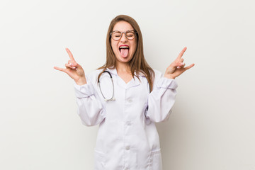 Young doctor woman against a white wall showing rock gesture with fingers