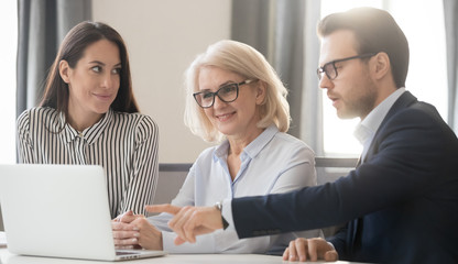 Fototapeta premium Businesspeople gather together in office sitting at desk using laptop