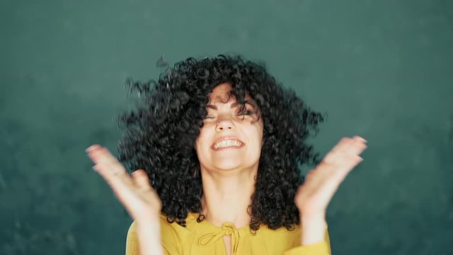 Funny curly haired girl shows yes gesture of victory, she managed to achieve result and goals. Surprised excited happy woman on green background