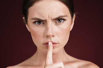 Naklejka premium Image of frowning shirtless woman holding finger at her lips