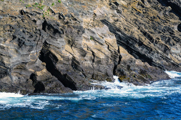 Waves of the turquoise sea crash against rocks of volcanic origin on the island of San Miguel,...