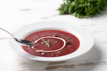 Delicious beet soup with sour cream in a white plate on white wooden table background. Soft light. Traditional Ukrainian Russian borscht beetroot soup