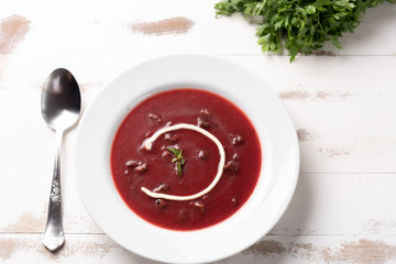 Delicious beet soup with sour cream in a white plate on white wooden table background. Soft light. Traditional Ukrainian Russian borscht beetroot soup
