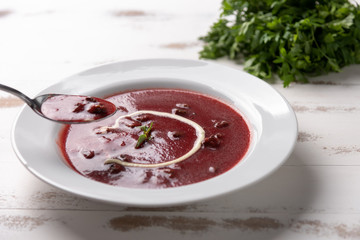 Delicious beet soup with sour cream in a white plate on white wooden table background. Soft light. Traditional Ukrainian Russian borscht beetroot soup