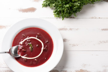 Delicious beet soup with sour cream in a white plate on white wooden table background. Soft light. Traditional Ukrainian Russian borscht beetroot soup