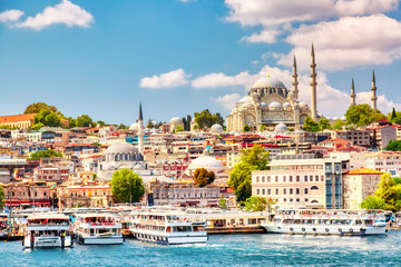 Fototapeta premium Turystyczne statki wycieczkowe w zatoce Golden Horn w Stambule i widok na meczet Sulejmana Wspaniałego z dzielnicą Sultanahmet na tle błękitnego nieba i chmur. Stambuł, Turcja w słoneczny letni dzień.