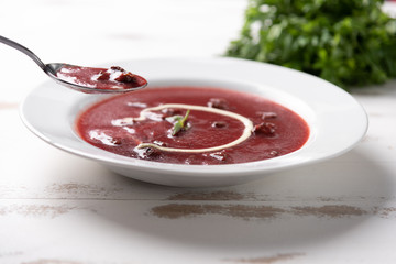 Delicious beet soup with sour cream in a white plate on white wooden table background. Soft light. Traditional Ukrainian Russian borscht beetroot soup