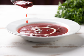 Delicious beet soup with sour cream in a white plate on white wooden table background. Soft light. Traditional Ukrainian Russian borscht beetroot soup