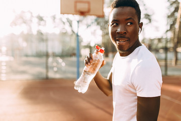 Young athletic African-American, at a sports stadium, holding a bottle of water - obrazy, fototapety, plakaty