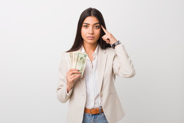 Young arab business woman holding dollars pointing his temple with finger, thinking, focused on a task.