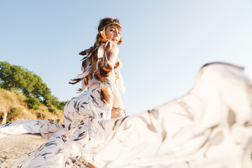 Fototapeta na wymiar Image of hippie girl wearing feather headband walking by seaside