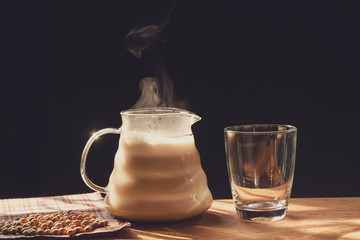 The steam from a jug of soy milk on the old wood table and black background, Warm drinks make good healthy, Made from soybeans, It is homemade food that is easy to make, Selective focus.