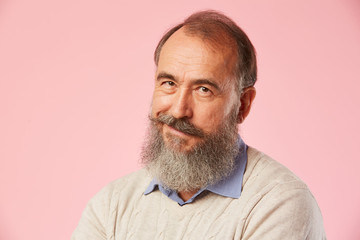 Fototapeta premium Close-up of mature man with grey beard smiling at camera over pink background