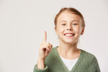 Portrait of happy little girl raising her finger up and smiling at camera over white background