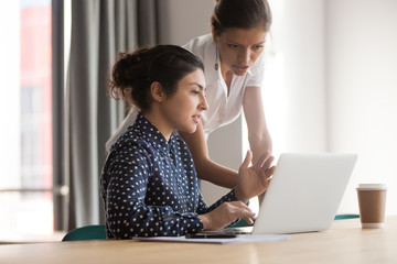 Diverse female mentor and intern talking pointing on laptop