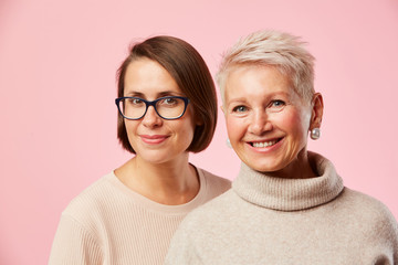 Portrait of beautiful young woman and mature woman standing together and smiling at camera against the pink background