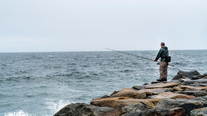 Fototapeta na wymiar Atlantic ocean rocky coastline of New York beach with fisherman.
