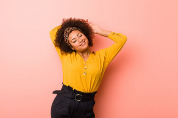 Young african american woman against a pink background stretching arms, relaxed position.