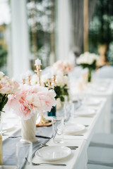 White long set wedding dinner table with decoration, candlestick, glasses, and flowers. Selective focus.