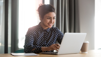 Happy young indian businesswoman using computer sit at office desk