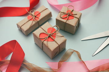 Process of packing presents in gift boxes. Craft paper, scissors, hemp threads, red satin ribbon. Gift wrapping.	